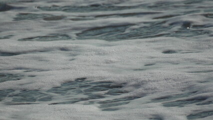 Foam Ocean Waves: White sea foam churning and receding in the ocean water on a bright sunny day.