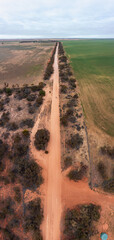 Aerial view of a long, straight sandy road cutting through the dry Mallee landscape near Walpeup, Victoria, bordered by native scrub and farmland under a bright sky. 