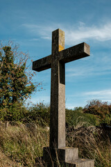 Stone cross standing in overgrown cemetery against blue sky