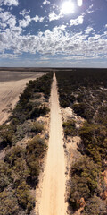Aerial view of a long, straight sandy road cutting through the dry Mallee landscape near Walpeup, Victoria, bordered by native scrub and farmland under a bright sky. 