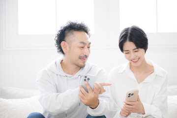 Obraz premium リビングでスマホを見るミドルの笑顔の夫婦やカップル