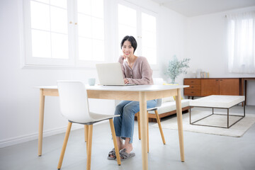 リビングでパソコンを使うニットを着た女性	カメラ目線の全身