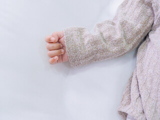 Close up of newborn baby hand is wearing a grey sweater on white rugs
