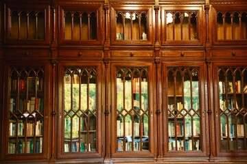 Vintage library interior with a large antique wooden bookshelf filled with many old books. Cozy warm atmosphere with classic architecture and timeless charm. Perfect for concepts of knowledge, history