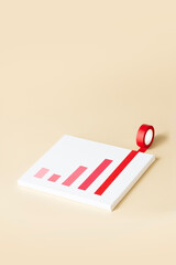 Conceptual success graph still life on cream colour background. One red tape rolling out from a white canvas background.