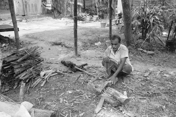 This image beautifully depicts a humble countryside moment where an old man is cutting wood with a hand axe amid natural surroundings, representing simplicity and sustainability.