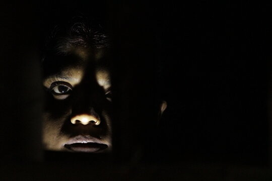 Artistic woman&rsquo;s face lit in darkness, expressing resilience, life, and emotion through shadow and subtle human expression.