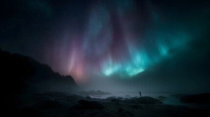 A lone person silhouetted on a rocky coast observes the vibrant Aurora Borealis illuminating the night sky with colorful lights