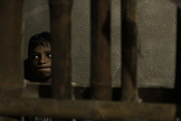 Artistic low-key shot of a boy behind a bamboo wall, capturing dramatic shadows, emotional intensity, and the silent narrative of struggle and hope.