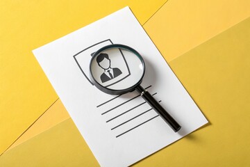 Magnifying glass examining a candidate profile on white paper