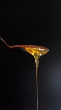 Thick golden honey flows smoothly from a spoon on a black background. Macro photography for cooking and advertising, the concept of a natural sweet product and mouth-watering texture.
