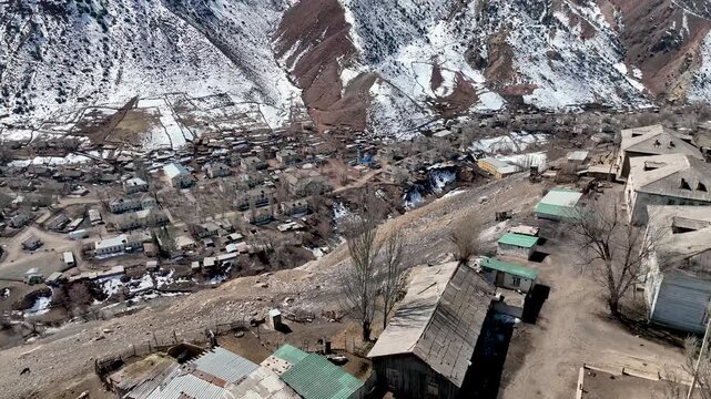 Elevated view of old, dilapidated wooden and asbestos roofed houses and outbuildings in the remote former Soviet uranium mining village nestled in a snowy mountain valley