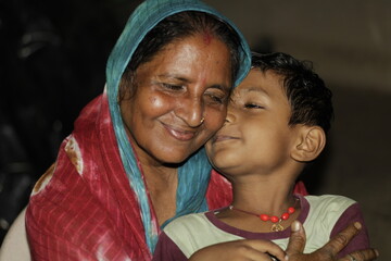 A loving grandmother smiles with her eyes closed as she hugs heR grandchildren, reflecting...