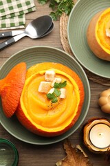 Tasty pumpkin cream soup with parsley and croutons served in pumpkin on wooden table, flat lay
