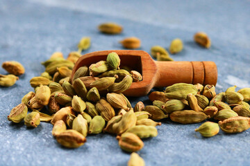 Heap of green cardamom seeds with wooden scoop on blue background