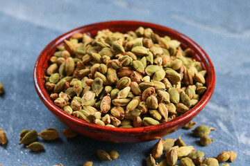 Heap of dried cardamom seeds in bowl on blue background