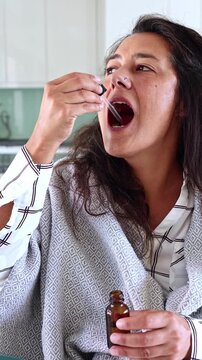 Sick woman taking liquid medicine with dropper at home