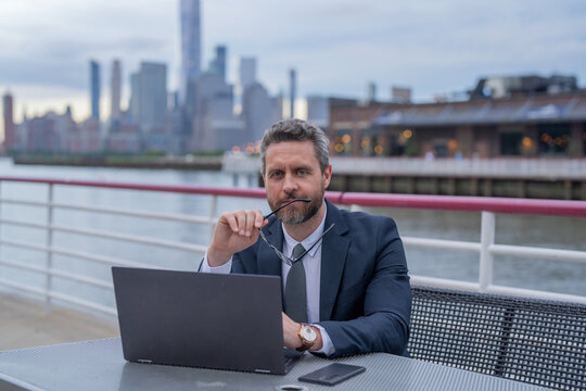 Middle eastern millennial business man in suit working on laptop outdoor. Mature handsome businessman working on his laptop outside in NY. Confident Entrepreneur using PC on the street.