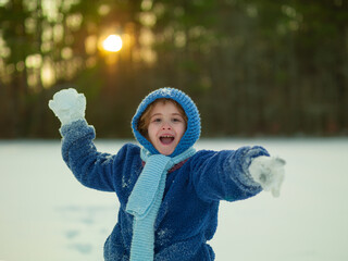Playful kid making and throwing snowballs. Child during snowball fight outdoors. Winter happiness....