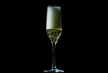 Sparkling wine splash in elegant wineglass. Champagne drink with golden fizz on black background.