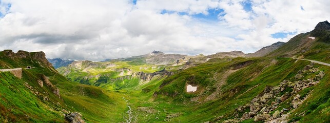 Discover the stunning beauty of a mountain pass, with green alpine meadows leading to majestic...