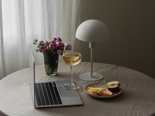 A cozy home aperitif - a glass of wine, cheese, an apple, a laptop on a round table with a gray tablecloth