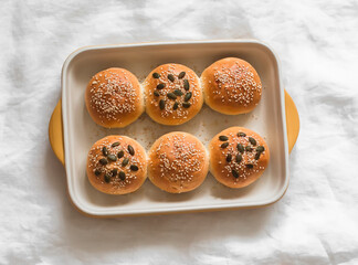Buns with pumpkin and sesame seeds in a baking dish on a light background, top view