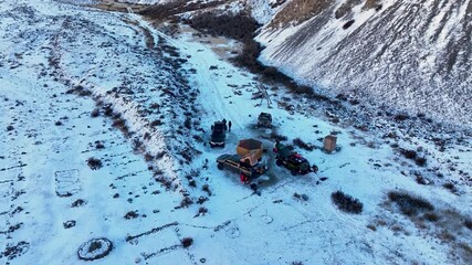 Kel Suu, Kyrgyzstan - October 13, 2024: Overhead aerial view of a small overlanding campsite with multiple 4x4 vehicles and tents set up in a desolate mountain valley dusted with early season snow