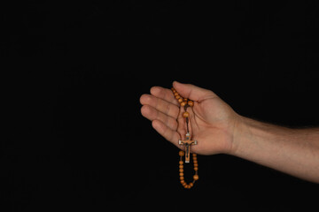 Hand holding wooden rosary beads against dark background