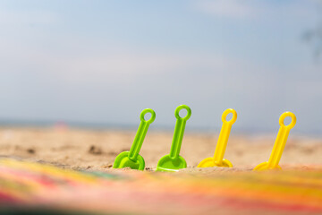 Colorful plastic sand shovels lined up on sunny tropical beach with soft sky background and wide...