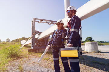 Engineers in safety gear conduct a detailed inspection of wind turbine blades at a construction site. Large blades are placed on the ground, highlighting the renewable energy technology.