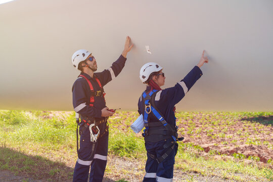 An engineer carefully examines a wind turbine blade at a construction site, placing a large blade on the ground to highlight the renewable energy technology.