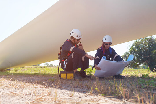 An engineer carefully examines a wind turbine blade at a construction site, placing a large blade on the ground to highlight the renewable energy technology.