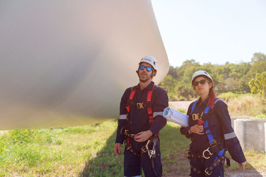 An engineer carefully examines a wind turbine blade at a construction site, placing a large blade on the ground to highlight the renewable energy technology.