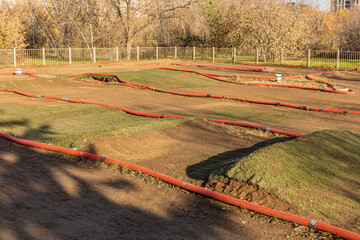 Outdoor remote-control car dirt track, bordered by red barriers and a fence. hobby, recreation, and outdoor activity.
