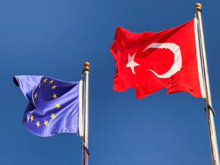 Turkish and European Union flags waving together against blue sky