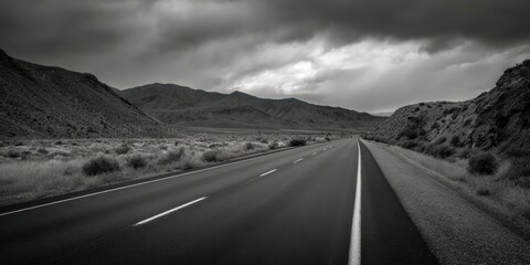 Dramatic monochrome landscape features a desolate highway stretching through mountains under a cloudy sky creating a sense of journey and isolation