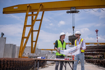 Naklejka premium Engineers wearing safety helmets and reflective vests working construction site large overhead crane operation ensure efficient secure handling of heavy materials industrial engineering project.