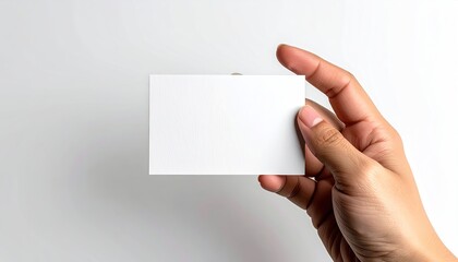 Obraz premium Close Up Of A Hand Holding A Blank White Business Card On A White Background With Soft Shadows Presenting A Clean Minimalist Aesthetic