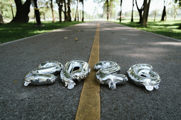 Silver balloons forming the number 2026 placed on a road with a yellow line, symbolizing a new journey, goal, and path toward the future.