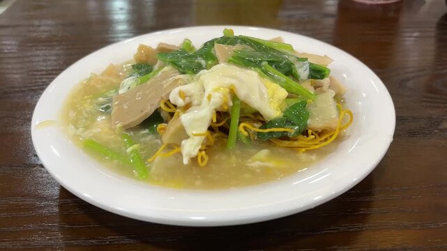 a plate of Capcay, an Indonesian-Chinese stir-fried vegetable dish, served with thick savory gravy, egg, and crispy noodles on a white plate. 