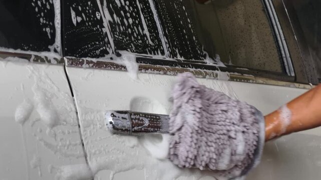 A man washes a white car with a soapy sponge.