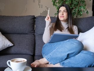 Woman relaxing on a couch, holding a digital tablet and stylus, finding creative inspiration