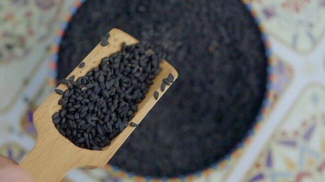 Black Cumin seeds pouring from a wooden spoon 