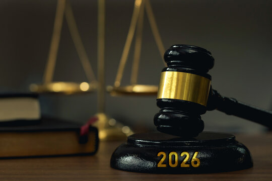 Close up judges gavel with gold band on a base engraved 2026, with blurred justice scales and a law book. Symbolizes law, court judgment, legal reform, governance, and the future justice system.
