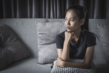 Young Asian woman sitting  on the sofa at home, feeling sad tired and worried suffering depression...