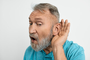 Obraz premium Close-up headshot of elderly man holding hand near his ear, isolated over white background. Hearing solutions