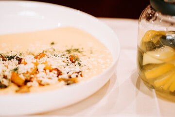 Delicious plate of creamy soup with herbs and vegetables beside a jar of lemon and cucumber water