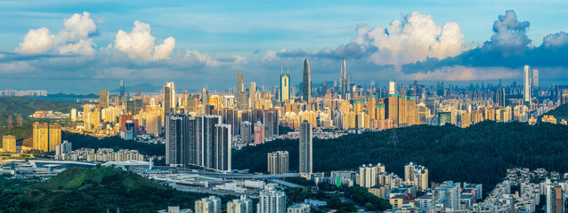Aerial panorama of the Shenzhen city skyline rising above green hills and urban residential districts at sunrise. © zhao dongfang