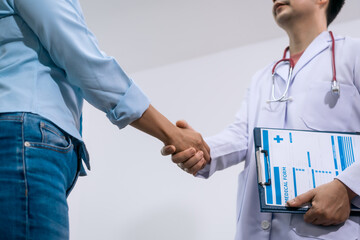 An Asian female patient with multiple injuries shakes hands with a male doctor in a clinic, showing...